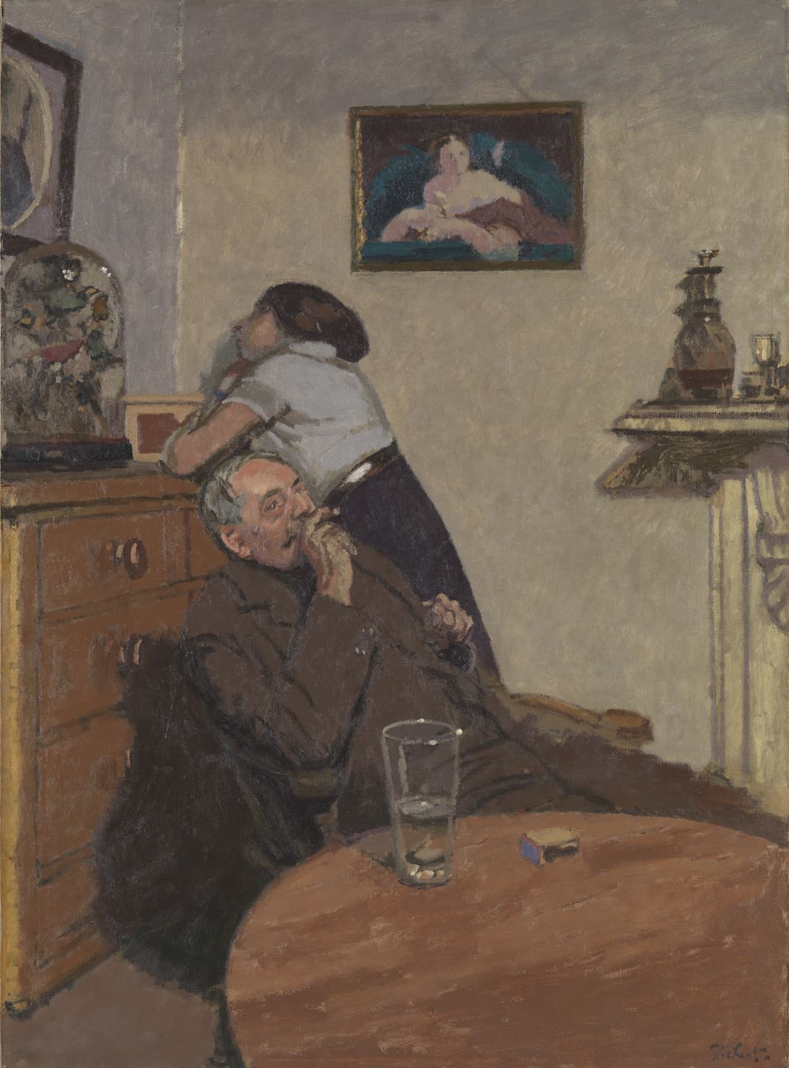 A man slumped at a table with a drink while a woman leans on a chest of drawers, both silent and bored